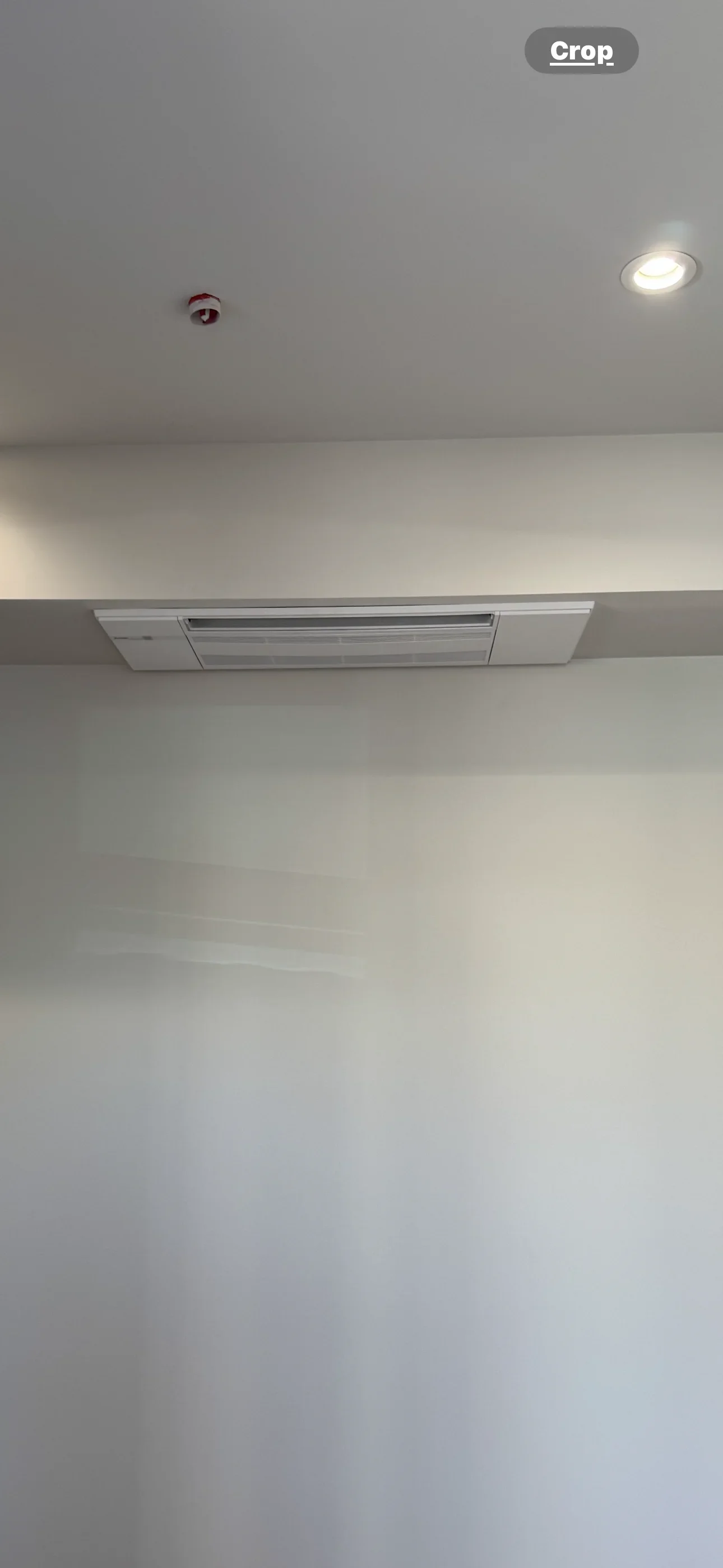 White ceiling-recessed ductless mini-split indoor unit with louvered grille mounted in a soffit beside a recessed downlight