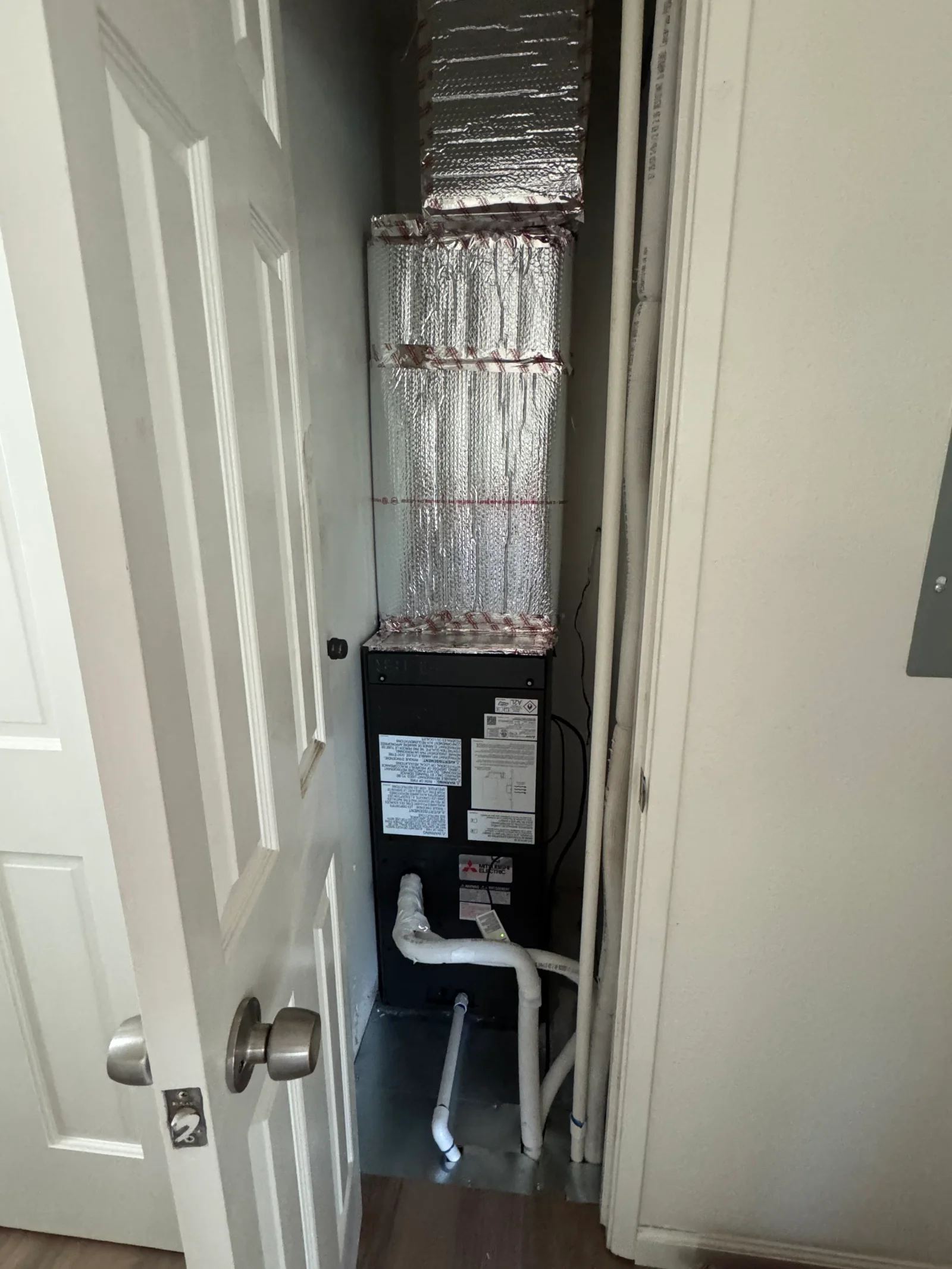 Mitsubishi Electric air handler with foil-wrapped ductwork and PVC condensate drain in utility closet