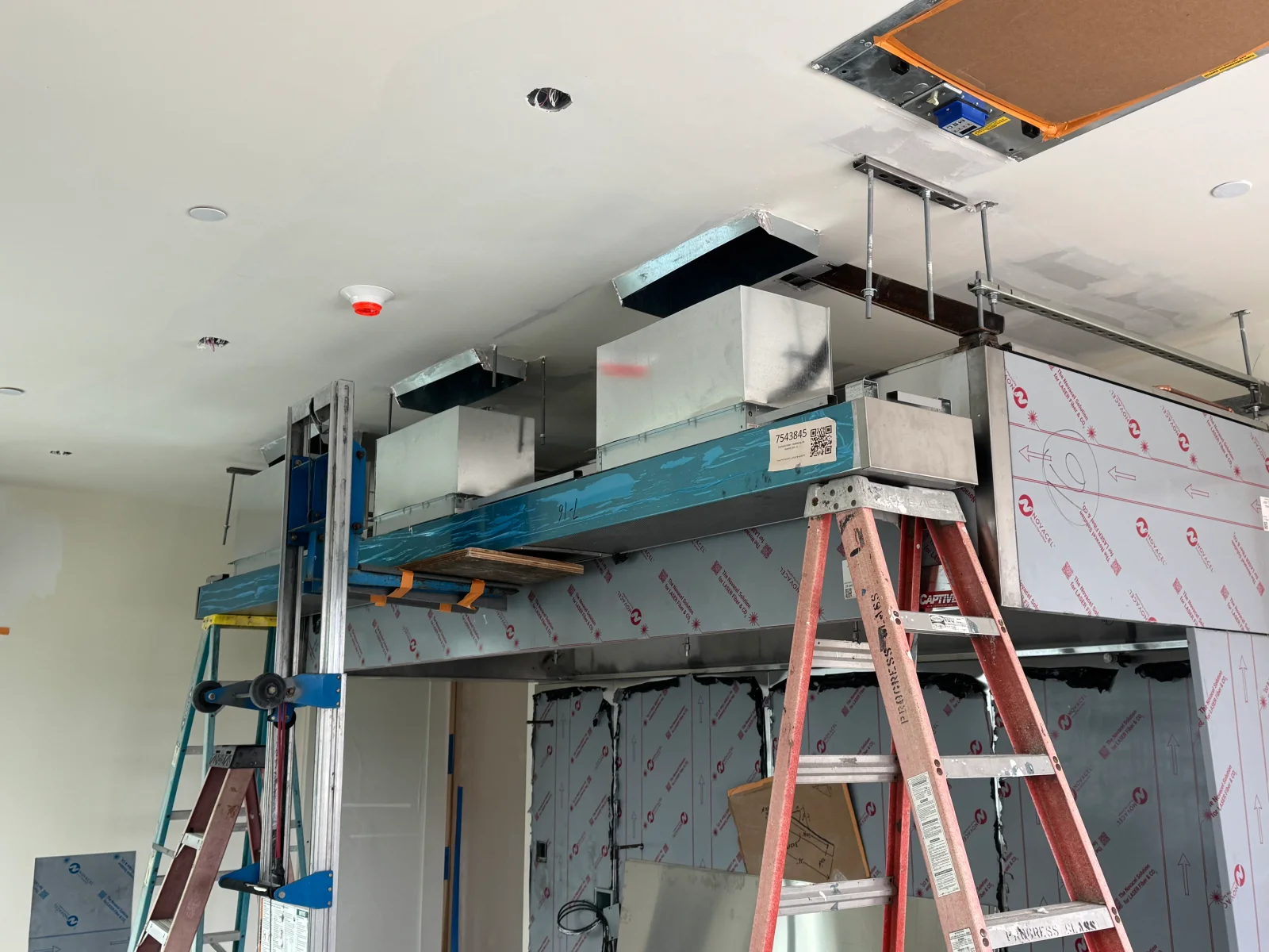 Overhead galvanized and blue-coated ductwork hung from threaded rods with protective wrap on stainless panels