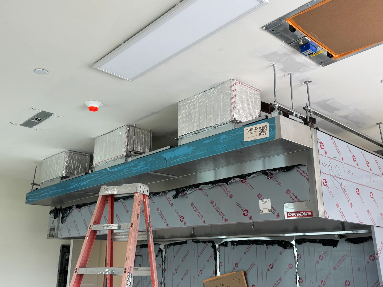 Stainless steel commercial kitchen exhaust hood with insulated ductwork and protective film during installation